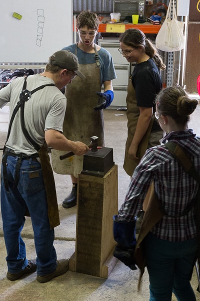 Male and female teenagers learning how to blacksmith